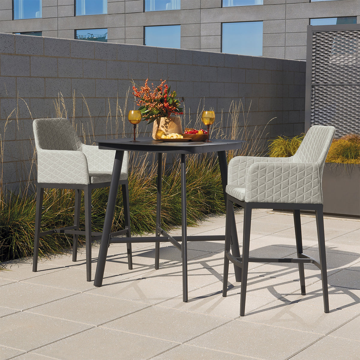 Two quilted upholstered bar chairs drawn up to a round outdoor bar table on a terrace