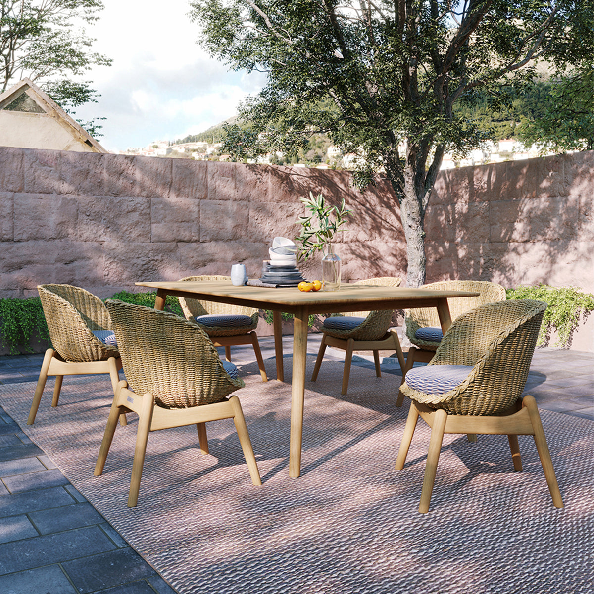 Long teak dining table set with pale woven dining chairs outdoors