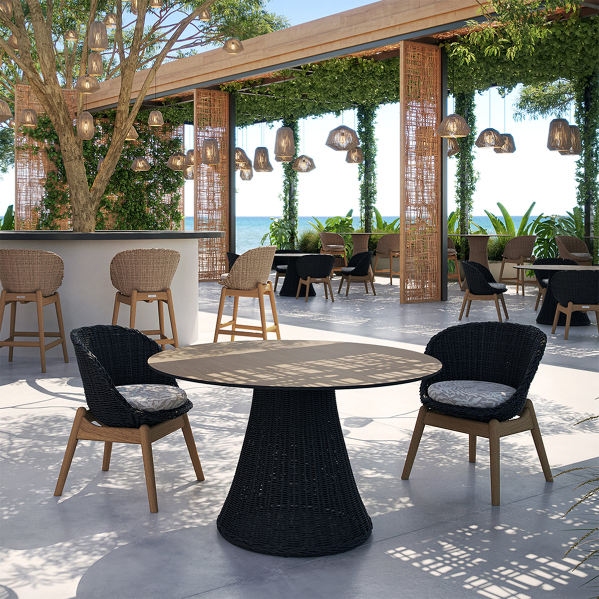Four woven dining chairs around a round pedestal table on a paved terrace