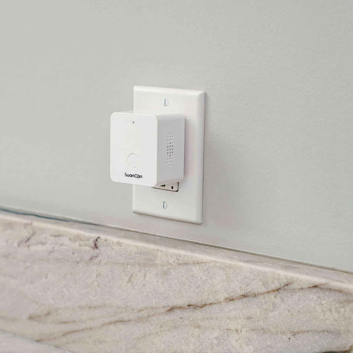 White alarm plugged into a wall outlet on a pale interior wall