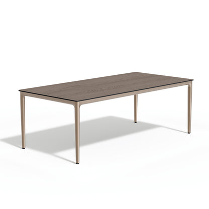 Long rectangular outdoor dining table with a wood toned laminate top on a slim aluminum frame, on a plain white background