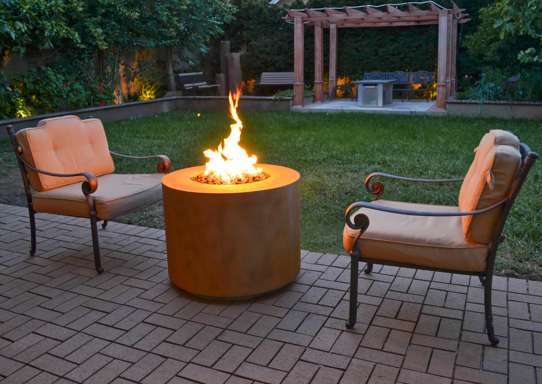The Outdoor Plus corten steel fire pit lit between two lounge chairs on a patio