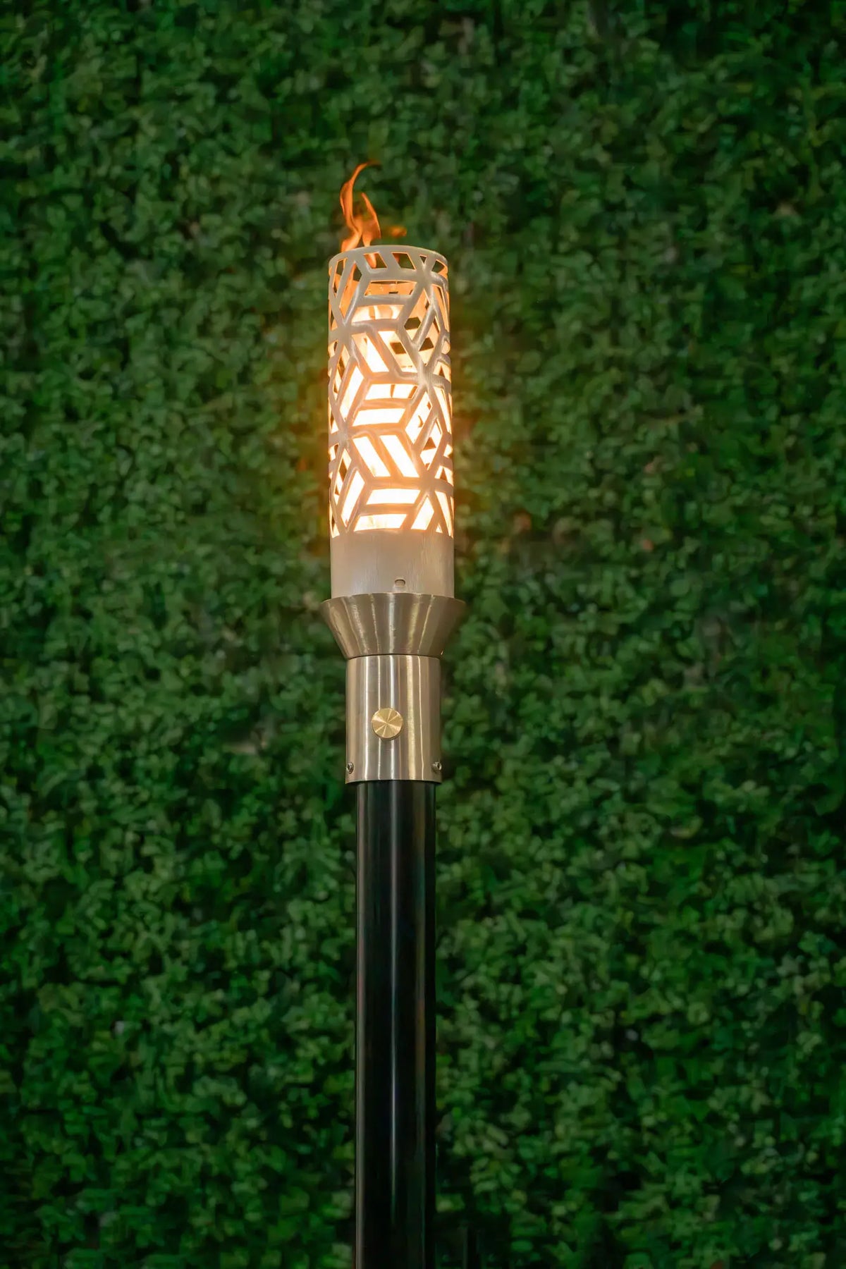 A lit stainless steel TOP Torch on a post against dark evening planting