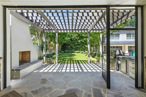 White brick outdoor fireplace under a pergola beside an outdoor kitchen